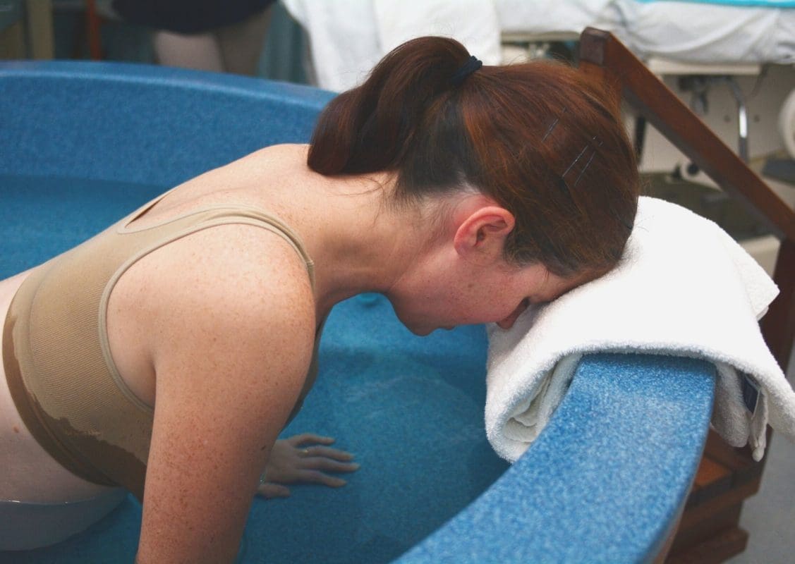 Frau während Wassergeburt im Vierfüßlerstand in Wanner